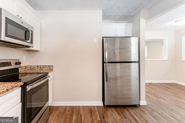 kitchen with light stone countertops, white cabinetry, appliances with stainless steel finishes, and a textured ceiling