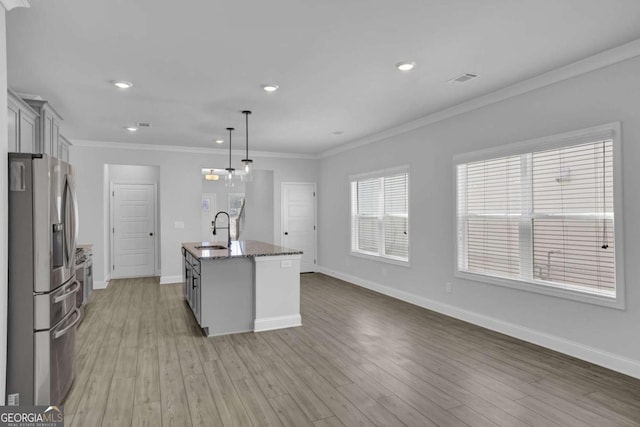 kitchen with stainless steel fridge with ice dispenser, hanging light fixtures, sink, dark stone countertops, and a center island with sink