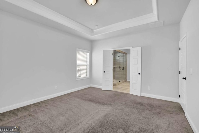 unfurnished bedroom with ensuite bathroom, light colored carpet, and a tray ceiling