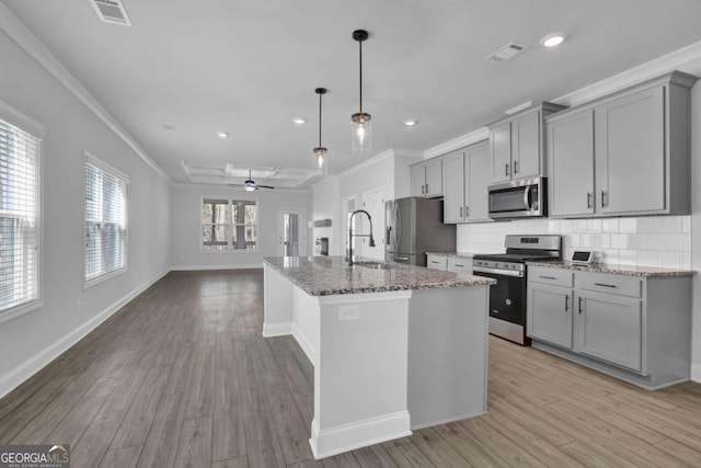 kitchen featuring light stone countertops, appliances with stainless steel finishes, a kitchen island with sink, gray cabinetry, and decorative light fixtures