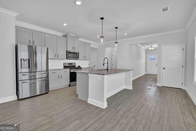 kitchen featuring dark stone counters, hanging light fixtures, stainless steel appliances, a center island with sink, and gray cabinets