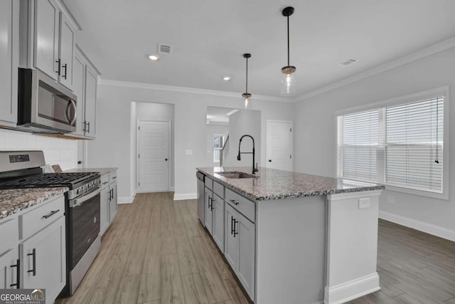 kitchen with light hardwood / wood-style flooring, hanging light fixtures, sink, a center island with sink, and stainless steel appliances