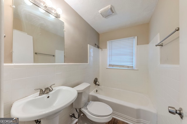 full bathroom with a textured ceiling, tiled shower / bath combo, sink, tile walls, and toilet