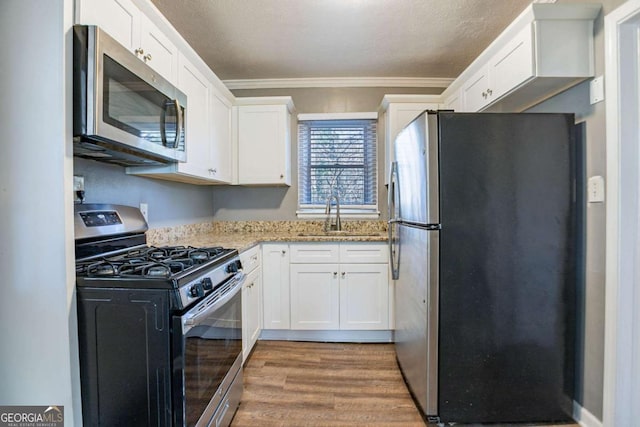 kitchen with ornamental molding, white cabinetry, light stone countertops, and appliances with stainless steel finishes