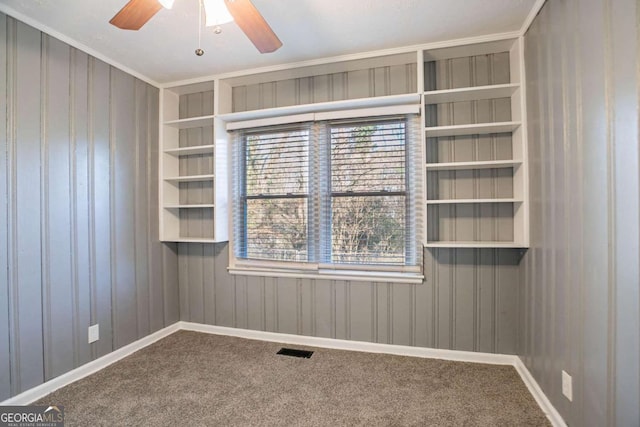 carpeted empty room with built in shelves, plenty of natural light, ceiling fan, and crown molding