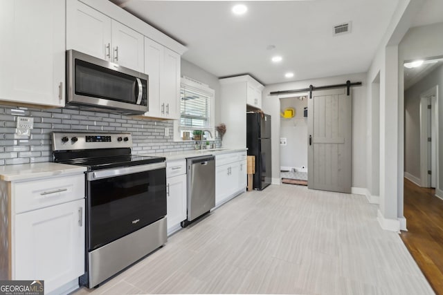 kitchen featuring appliances with stainless steel finishes, sink, backsplash, white cabinets, and a barn door