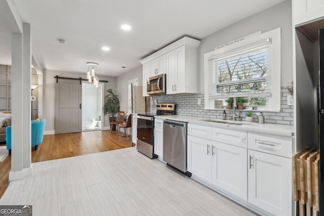 kitchen with tasteful backsplash, white cabinetry, a barn door, sink, and stainless steel appliances