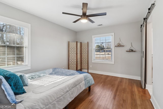 bedroom with ceiling fan, wood-type flooring, and a barn door