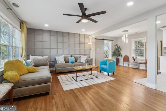 living room with light hardwood / wood-style flooring, ceiling fan, and a barn door