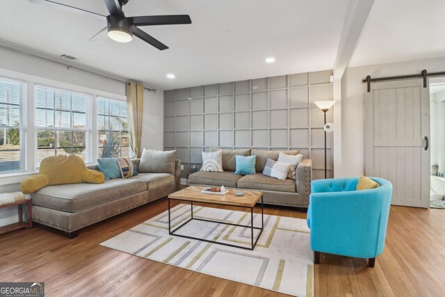 living room featuring light wood-type flooring, ceiling fan, and a barn door