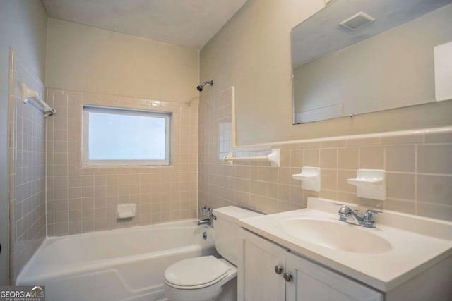 full bathroom featuring tiled shower / bath combo, toilet, tile walls, and vanity