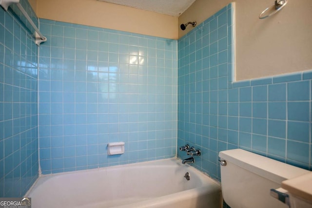 bathroom with toilet, a textured ceiling, tile walls, and bathing tub / shower combination