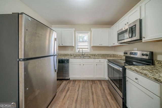 kitchen with sink, hardwood / wood-style flooring, white cabinetry, light stone counters, and stainless steel appliances