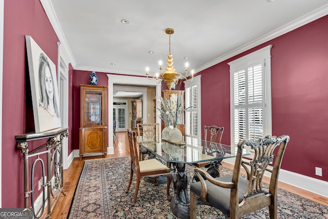 dining room with hardwood / wood-style flooring, crown molding, and a notable chandelier