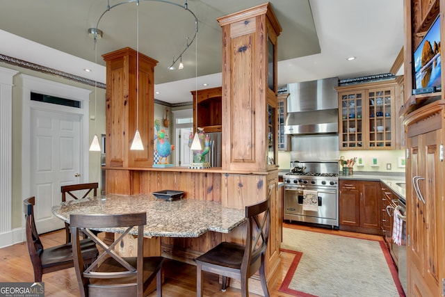 kitchen featuring decorative columns, designer range, kitchen peninsula, light wood-type flooring, and wall chimney exhaust hood