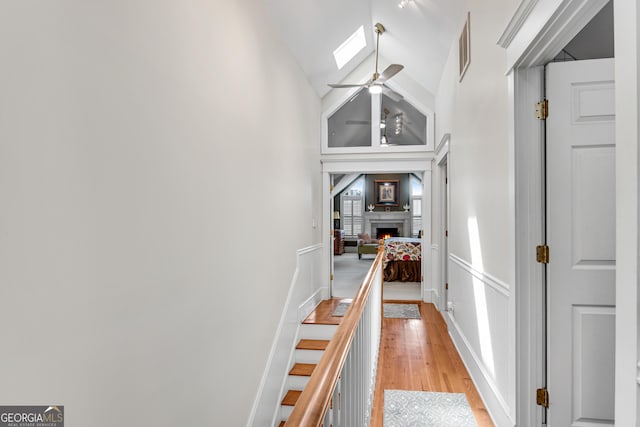 hallway featuring high vaulted ceiling, a skylight, and light hardwood / wood-style floors