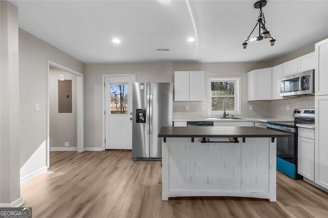 kitchen with appliances with stainless steel finishes, decorative light fixtures, sink, white cabinets, and a kitchen island