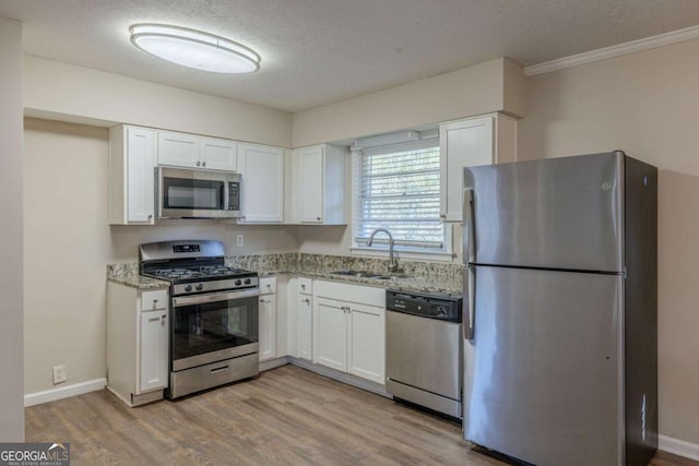 kitchen with sink, white cabinets, light stone counters, a textured ceiling, and stainless steel appliances