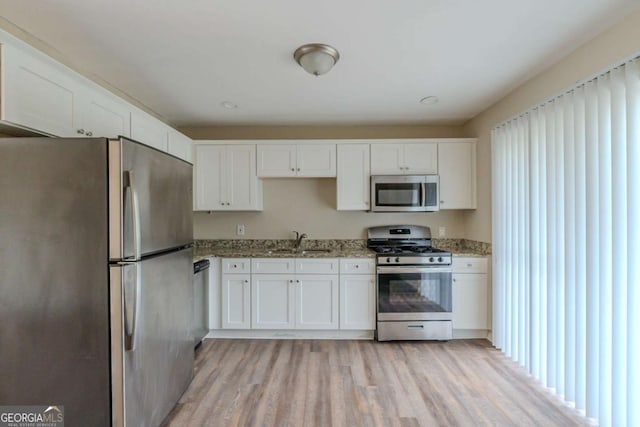 kitchen featuring light hardwood / wood-style floors, light stone countertops, appliances with stainless steel finishes, white cabinets, and sink