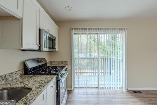 kitchen featuring light stone countertops, light hardwood / wood-style floors, white cabinetry, and appliances with stainless steel finishes