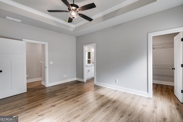 unfurnished bedroom with a tray ceiling, light hardwood / wood-style flooring, and a spacious closet