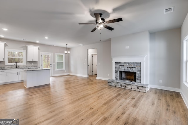 unfurnished living room with sink, ceiling fan with notable chandelier, a fireplace, and light hardwood / wood-style flooring