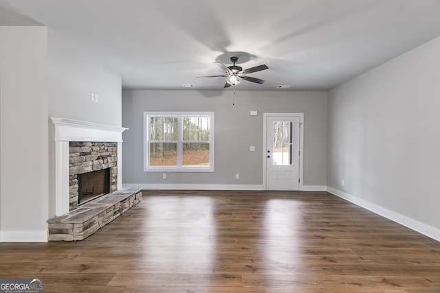 unfurnished living room with a stone fireplace, dark wood-type flooring, and ceiling fan