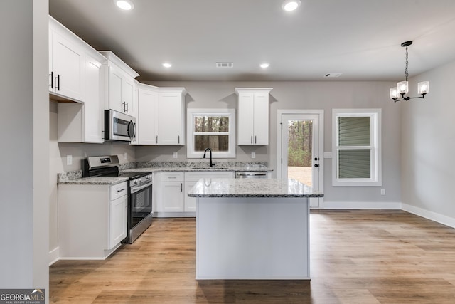 kitchen with sink, white cabinets, a center island, light stone counters, and stainless steel appliances