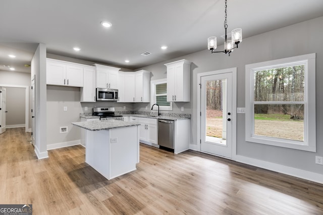 kitchen featuring white cabinetry, decorative light fixtures, a center island, appliances with stainless steel finishes, and light stone countertops