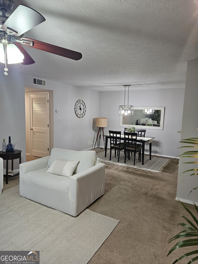 carpeted living area with a textured ceiling, visible vents, and a ceiling fan