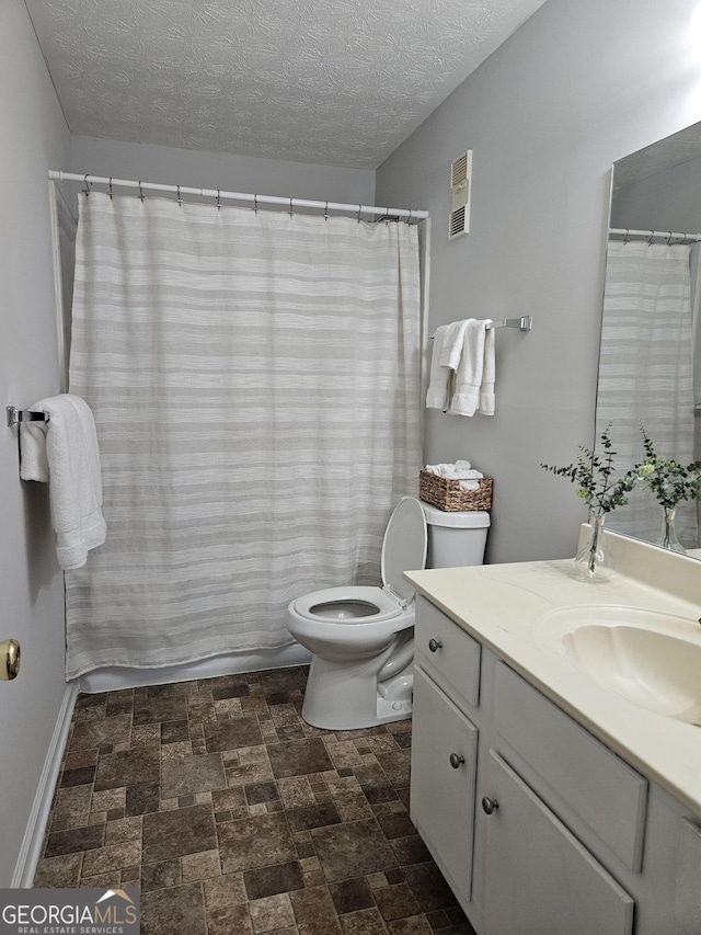 full bathroom with toilet, stone finish floor, vanity, a textured ceiling, and baseboards