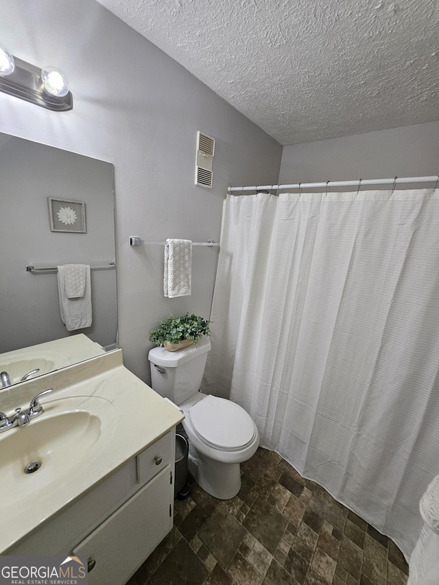 bathroom featuring a textured ceiling, toilet, vanity, visible vents, and stone finish flooring