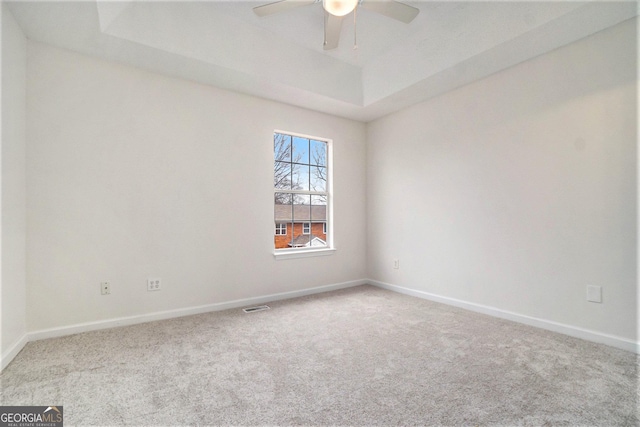 empty room with ceiling fan, a raised ceiling, and light carpet