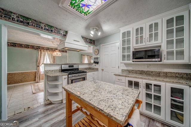 kitchen featuring pendant lighting, a center island, a textured ceiling, white cabinets, and gas range