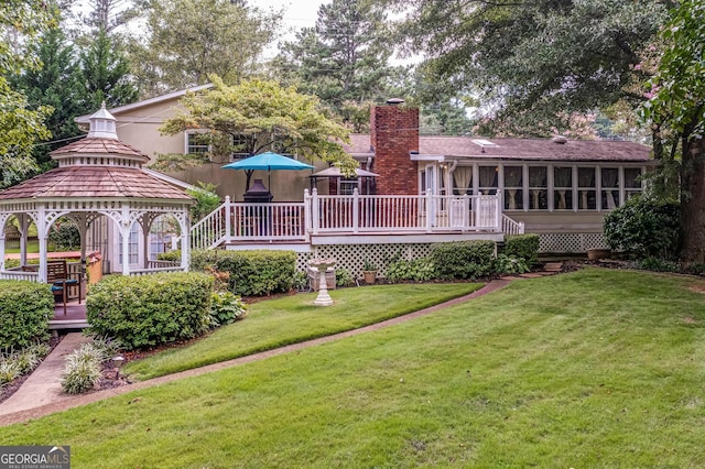 rear view of property with a gazebo, a sunroom, a deck, and a lawn