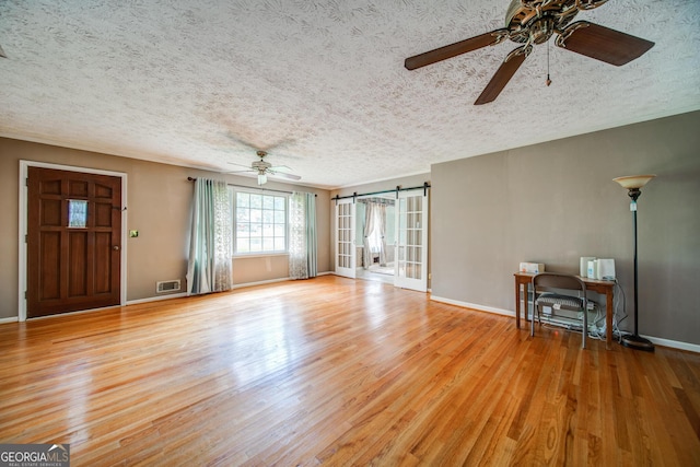 unfurnished living room featuring ceiling fan, wood-type flooring, a barn door, and a textured ceiling