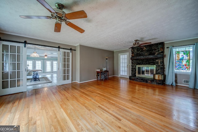 unfurnished living room with hardwood / wood-style flooring, ceiling fan, a textured ceiling, a stone fireplace, and a barn door