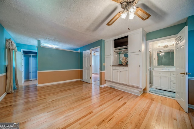 unfurnished bedroom featuring ceiling fan, connected bathroom, a textured ceiling, and light wood-type flooring