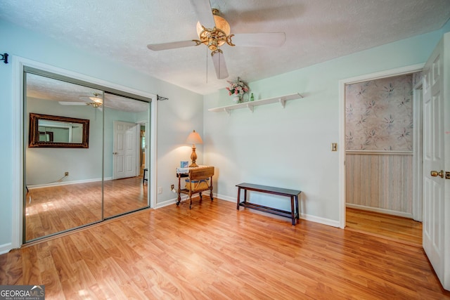 unfurnished bedroom featuring light hardwood / wood-style flooring, ceiling fan, a textured ceiling, a closet, and wood walls