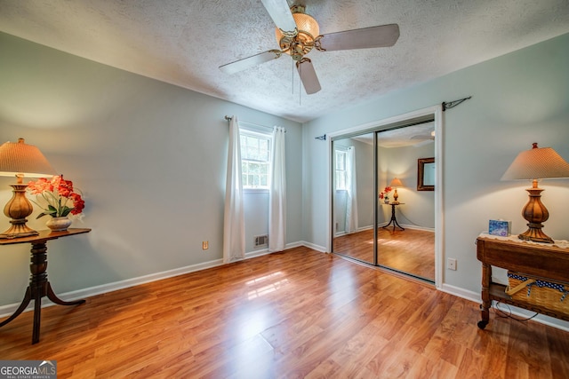 bedroom with ceiling fan, light hardwood / wood-style floors, a closet, and a textured ceiling