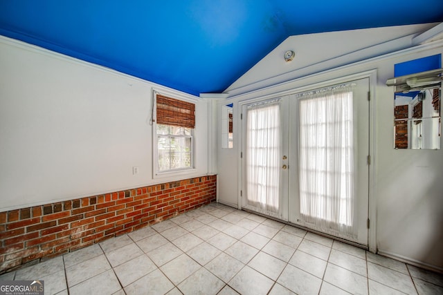 empty room featuring light tile patterned floors, vaulted ceiling, french doors, and brick wall