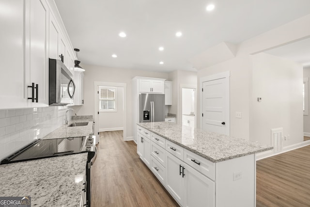 kitchen with sink, appliances with stainless steel finishes, light stone countertops, white cabinets, and a kitchen island