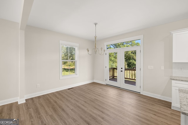 unfurnished dining area featuring hardwood / wood-style flooring, an inviting chandelier, and french doors