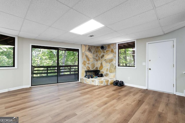 unfurnished living room featuring a paneled ceiling, a stone fireplace, and light hardwood / wood-style flooring