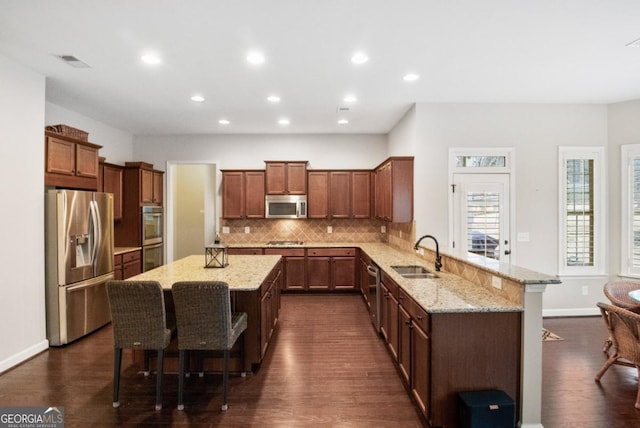 kitchen with a breakfast bar, sink, appliances with stainless steel finishes, a kitchen island, and light stone countertops