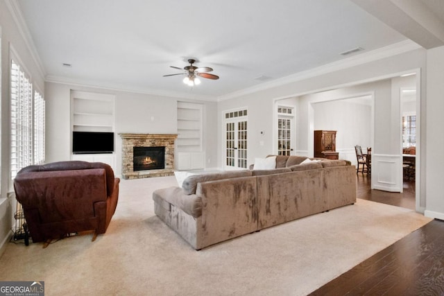 living room featuring built in shelves, crown molding, and a stone fireplace