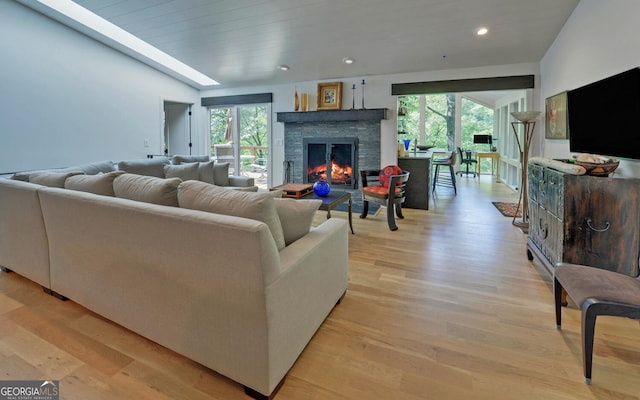 living room with a stone fireplace, light hardwood / wood-style flooring, and a wealth of natural light