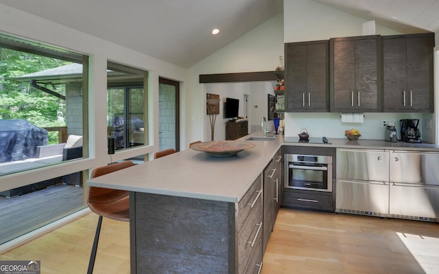 kitchen featuring sink, stainless steel oven, vaulted ceiling, a kitchen breakfast bar, and kitchen peninsula