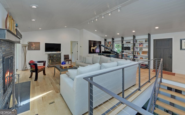 living room featuring rail lighting, a stone fireplace, lofted ceiling, and light hardwood / wood-style floors