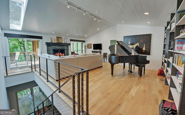 living room with rail lighting, a stone fireplace, lofted ceiling with skylight, wood ceiling, and light hardwood / wood-style flooring